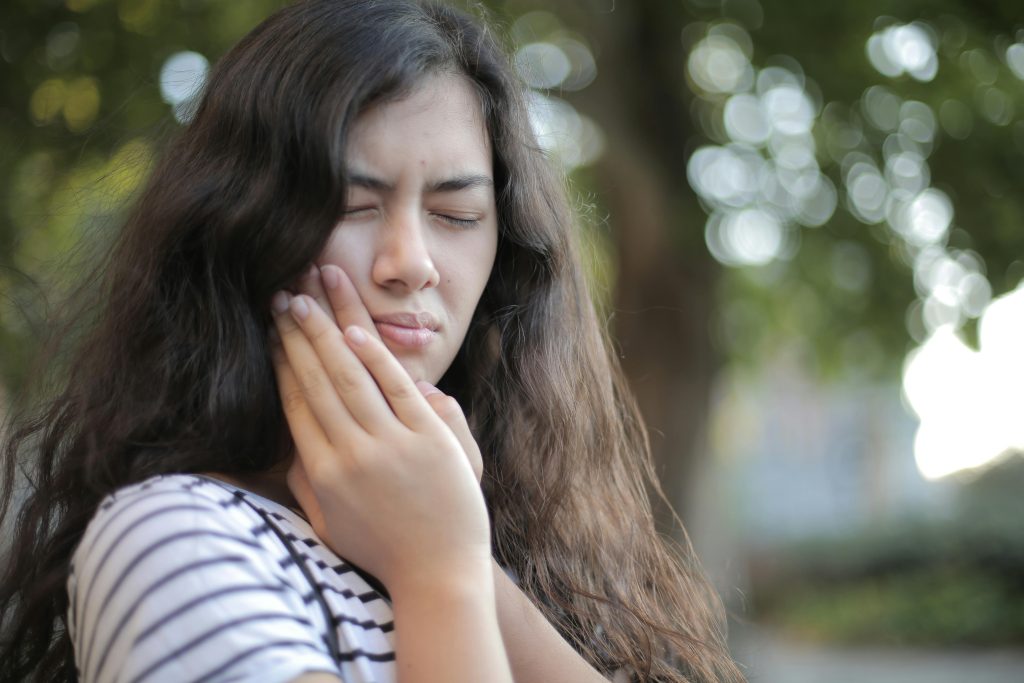 woman in pain, touching her jaw with both hands